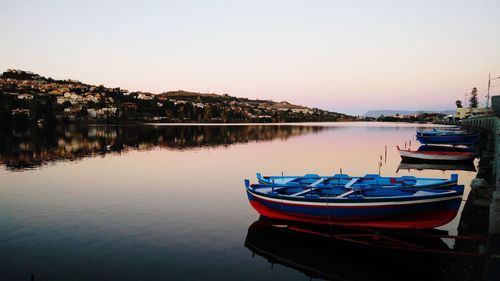 Boats moored in lake against sky during sunset