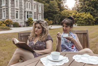 Couple of mature friendly women on vacation drinking tea and reading a book outdoors