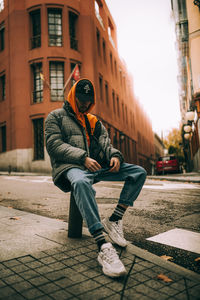 Full length of man sitting on street in city