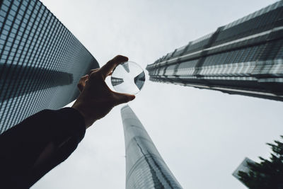 Close-up of hand holding office building against sky