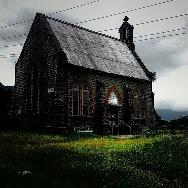 building exterior, architecture, built structure, church, sky, religion, low angle view, place of worship, grass, spirituality, outdoors, day, plant, no people, facade, green color, cross, field