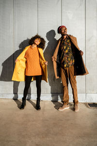 Full length of black african american couple in trendy vivid warm outfit standing with looking away with closed eyes on street