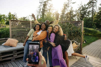 Hand of man photographing young male and female friends posing during party in back yard