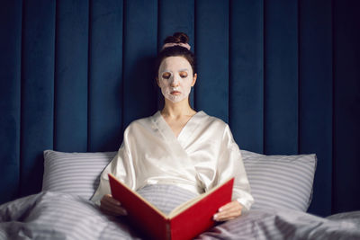 Woman applies cleansing mask on face. rejuvenating effect. sits on the bed and reads the red book