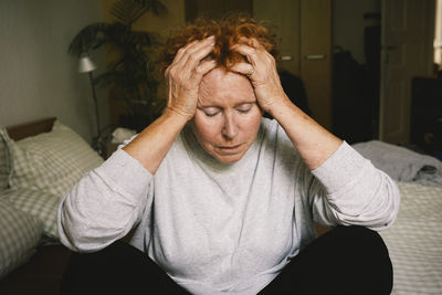 Depressed senior woman sitting with head in hands in bedroom