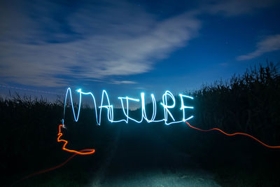 Close-up of illuminated text against sky at night