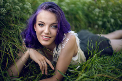 Portrait of a teenage girl with purple hair and an earring in her nose lying in the grass in nature