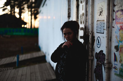 Portrait of young woman with hand on chin standing by cargo container