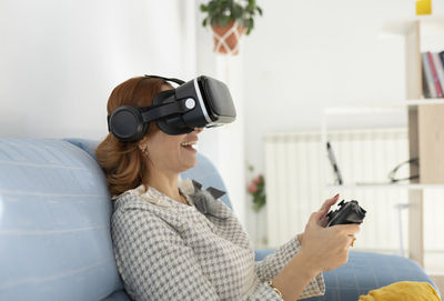 Woman holding joystick wearing virtual reality headset at home