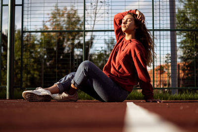 Side view of young woman with eyes closed sitting on sports track