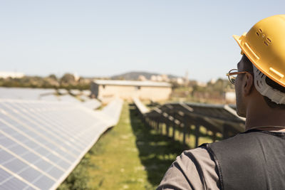 Male engineer wearing hardhat while looking at solar panels in field