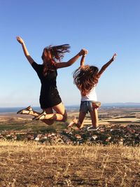 Friends jumping over land against clear sky