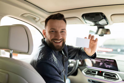 Portrait of smiling man showing placard in car