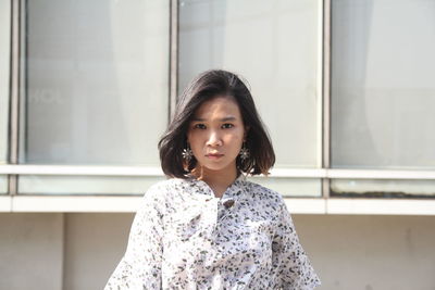 Portrait of woman standing against building on footpath