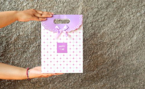 Close-up of hand holding paper bag with text against wall 