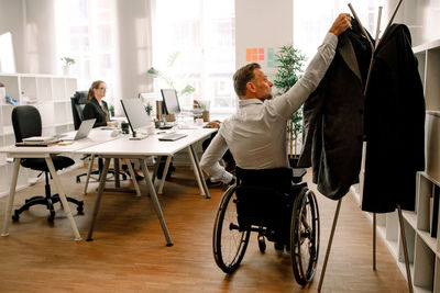 Rear view of disabled businessman hanging coat in office