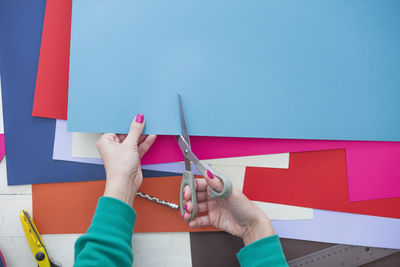 Cropped hands of woman cutting colorful papers on table