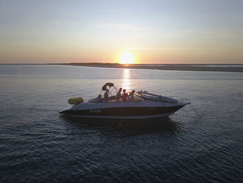 People on sea against sky during sunset