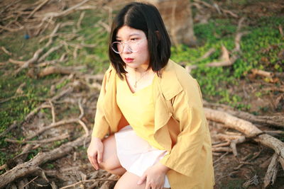 Young woman looking away while sitting on land