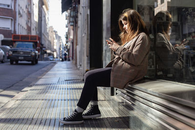 Woman sitting on sidewalk in city