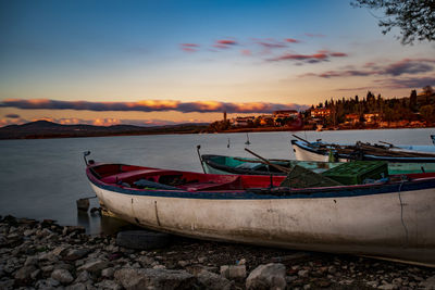 Boat moored on beach against sky during sunset