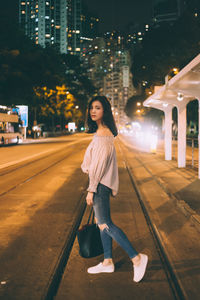 Young woman standing on footpath at night