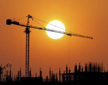 Silhouette cranes at construction site against sky during sunset