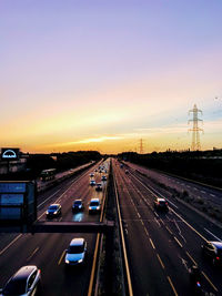 Vehicles on highway in city against sky during sunset