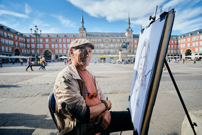 Man sitting in city against sky