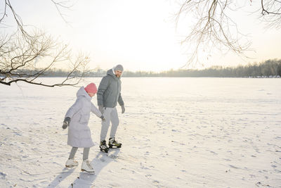 Father and daughter doing ice skating on frozen lake in winter