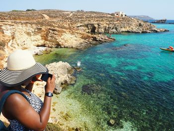 Woman photographing turquoise sea on sunny day