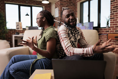 Friends using laptop while sitting on sofa at home