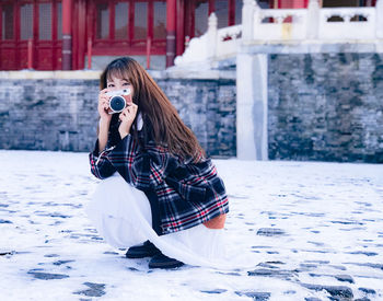 Woman photographing while sitting on snow