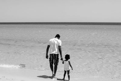 Rear view of father and daughter walking on shore at beach