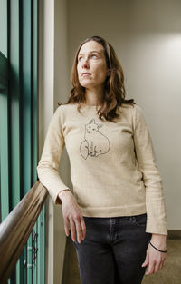 A woman with a serious expression leans on rail looking out a window