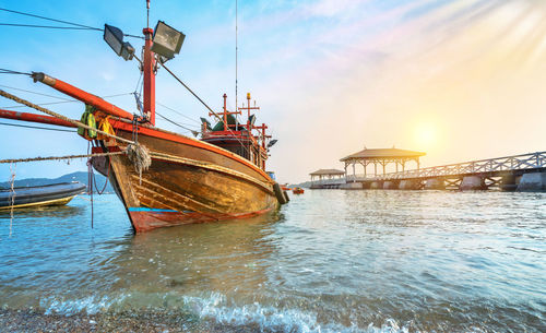 Fishing boat moored in sea against sky during sunset