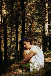 Side view of woman standing by tree trunk in forest