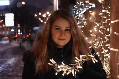 Portrait of beautiful woman standing by illuminated lights