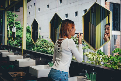 Woman applying lipstick while looking into mirror while standing in bathroom