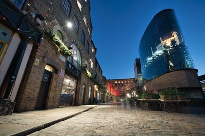 Illuminated street amidst buildings against sky at night