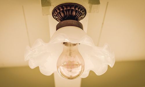 Low angle view of illuminated lamp hanging against wall at home