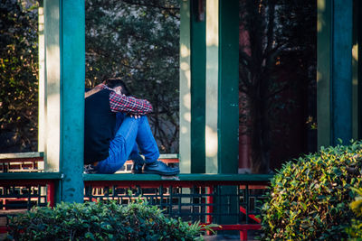 Full length of man sitting on seat against trees
