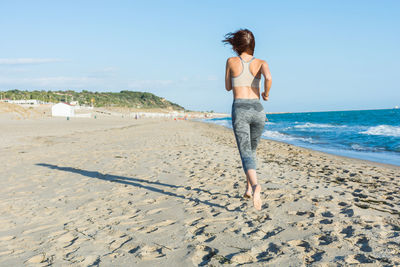 Full length of young woman on beach against clear sky