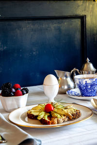 Avocado toast, mixed berries, tea and a soft boiled egg for breakfast on a table with a blue vase.