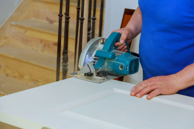 Midsection of carpenter cutting plank at home