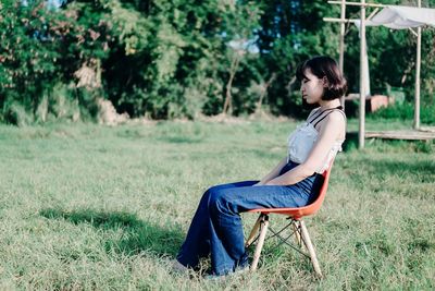 Side view of young woman sitting on chair at field