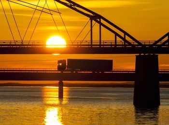 Silhouette bridge over sea against sky during sunset