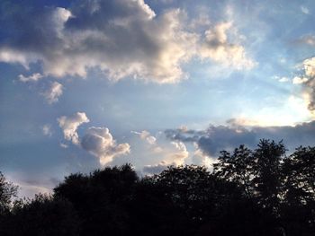 Low angle view of trees against cloudy sky