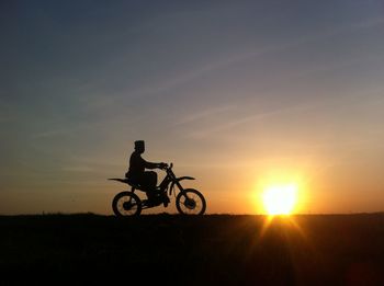 Silhouette man riding motorcycle on field against sky during sunset