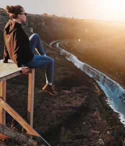 Woman sitting on table against land during sunset